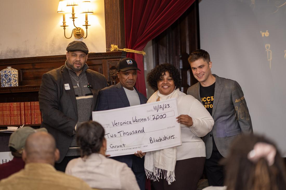 A grant recipient holds a $2,000 check with the R3SET team
